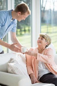 Carer handing an elderly woman a cup of tea